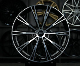 Close-up of a large black and silver multi-spoke alloy car wheel with an ABT center cap in a showroom backdrop of other rims.
