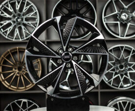 Close-up of a black and silver Audi alloy wheel on a display stand, with a wall of other rims in the background.