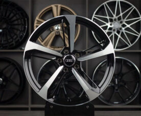Close-up of a black and silver Audi alloy wheel on display with other rims in the background.
