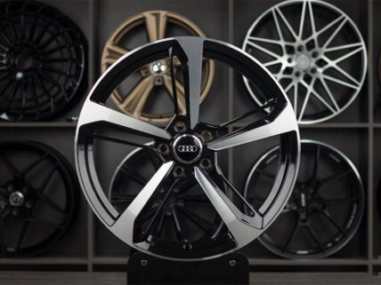 Close-up of a black and silver Audi alloy wheel on display with other rims in the background.