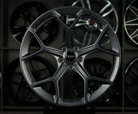 Close-up of a dark gray Audi alloy wheel with a five-spoke star design on display, with other wheels in the background.