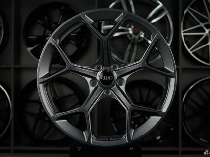 Close-up of a dark gray Audi alloy wheel with a five-spoke star design on display, with other wheels in the background.