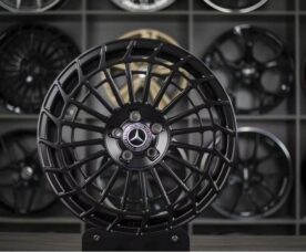 Black Mercedes-Benz alloy wheel with a complex lattice spoke design and center cap featuring the Mercedes logo on display stand.