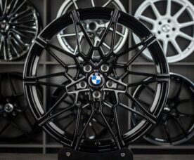 Black multi-spoke BMW alloy wheel on display with other rims in the background.