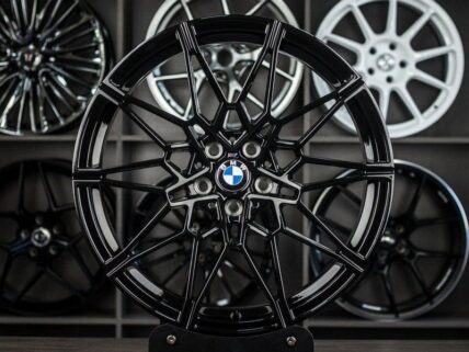 Black multi-spoke BMW alloy wheel on display with other rims in the background.