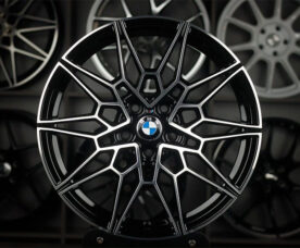 Close-up of a black and silver BMW alloy wheel with a complex multi-spoke pattern and BMW center cap in a showroom setting