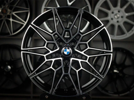 Close-up of a black and silver BMW alloy wheel with a complex multi-spoke pattern and BMW center cap in a showroom setting